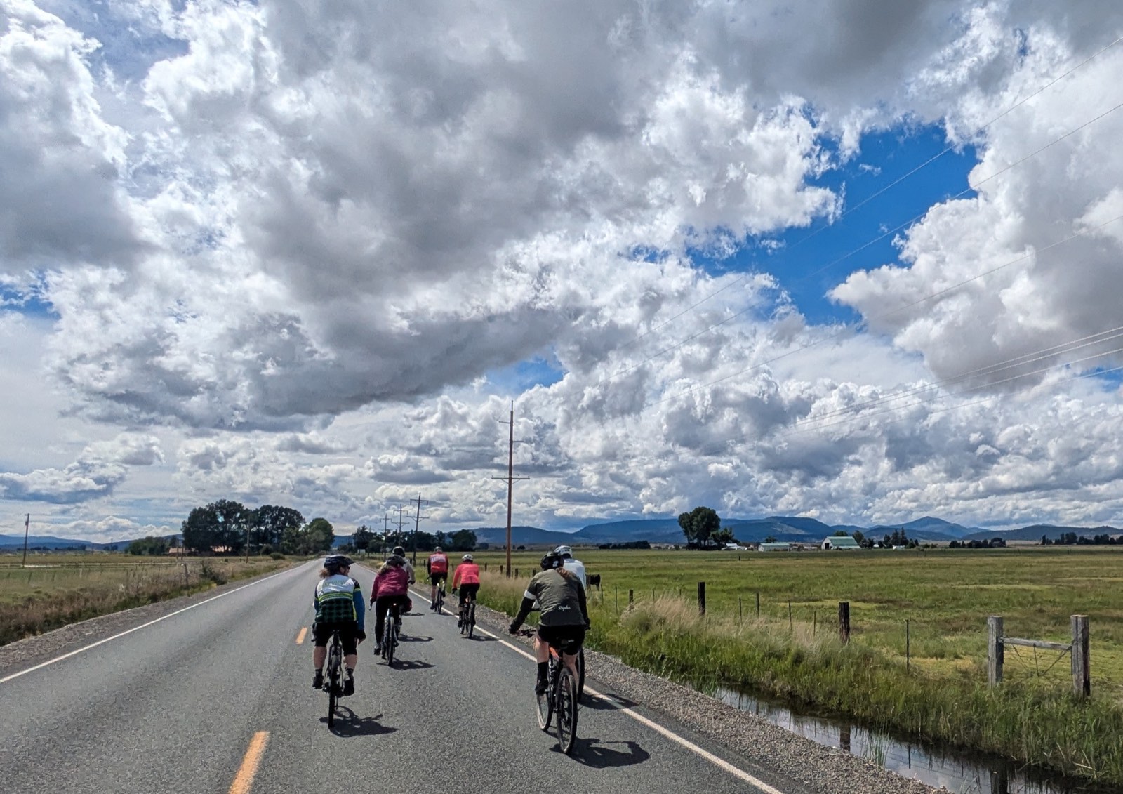 Riders on a farm road watching a massive bank of storm clouds building overhead