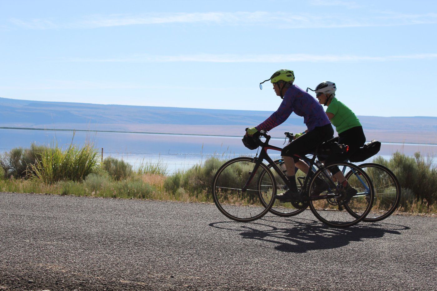 Cyclists riding past a lake with rimrock cliffs in the background near Lakeview, Oregon